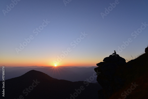 Silhouette of woman was sitting on the rocks in mountain for watching sun set.