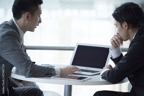Two businessmen have a meeting while looking at a laptop