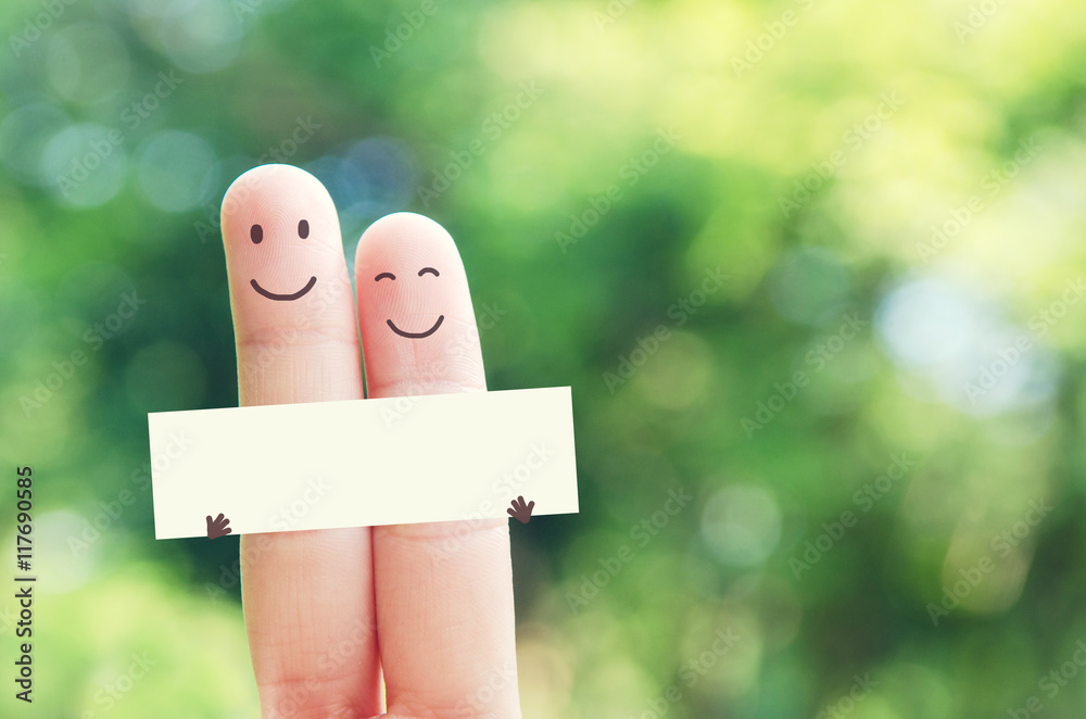 Fototapeta premium 2 fingers holding blank paper while smiling face with nature bokeh background. Paper empty for message and wording.