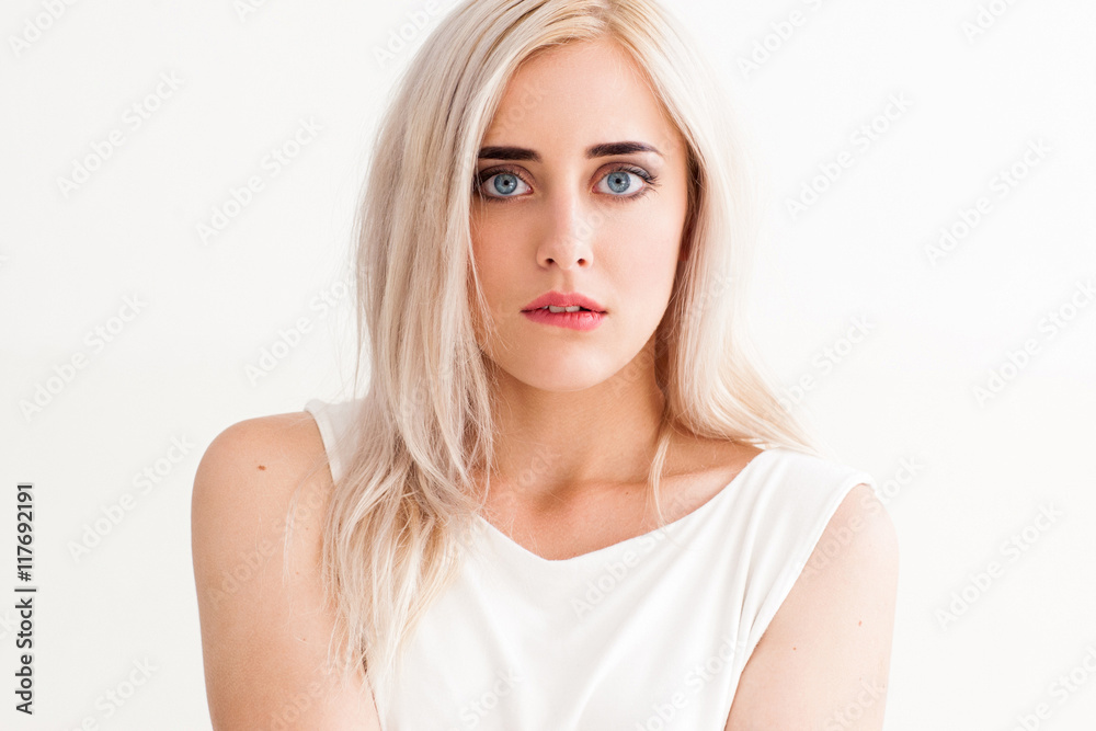 Surprised shocked blonde girl biting her lip with widely opened eyes. Amazed woman in light cloth on white background, free space Surprised shocked blonde girl biting her lip with widely opened eyes. Amazed woman in light cloth on white background, free space