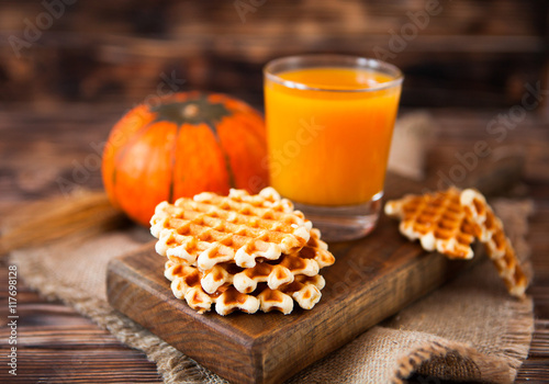 Glass of fresh pumpkin juice with wafer and pumpkin on dark wood