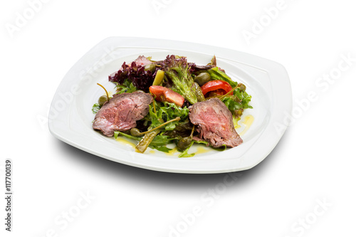 warm salad with beef slices of pickled cucumbers and capers on a white plate and a white background