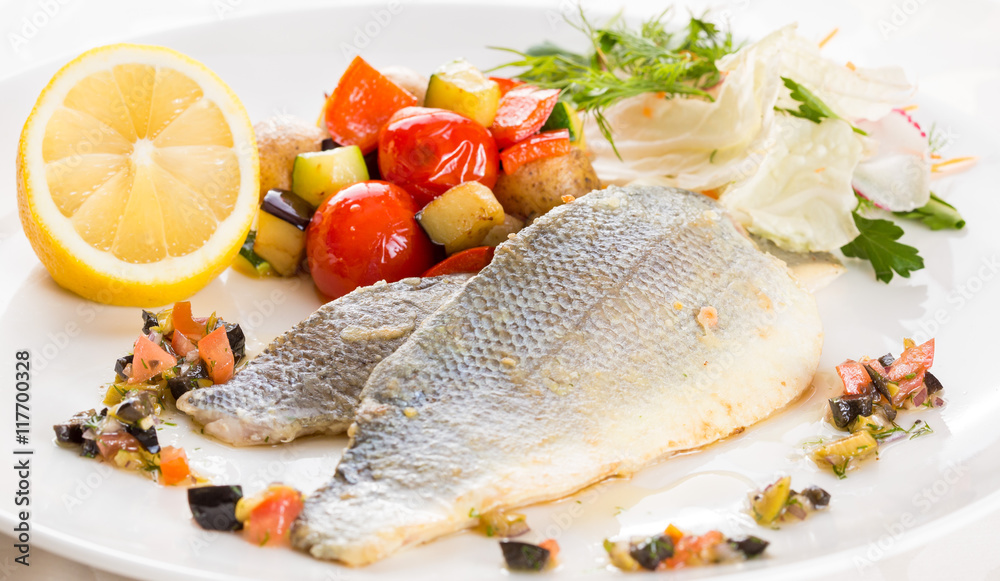Baked fish with vegetables and lemon. On a white plate Baked fish with vegetables and lemon. On a white plate