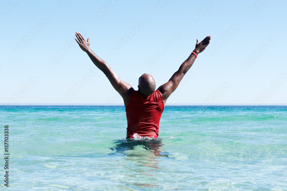 African man standing in sea with his hands raised African man standing in sea with his hands raised