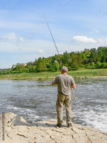 Fisherman back river bank long fishing rod green forest gray