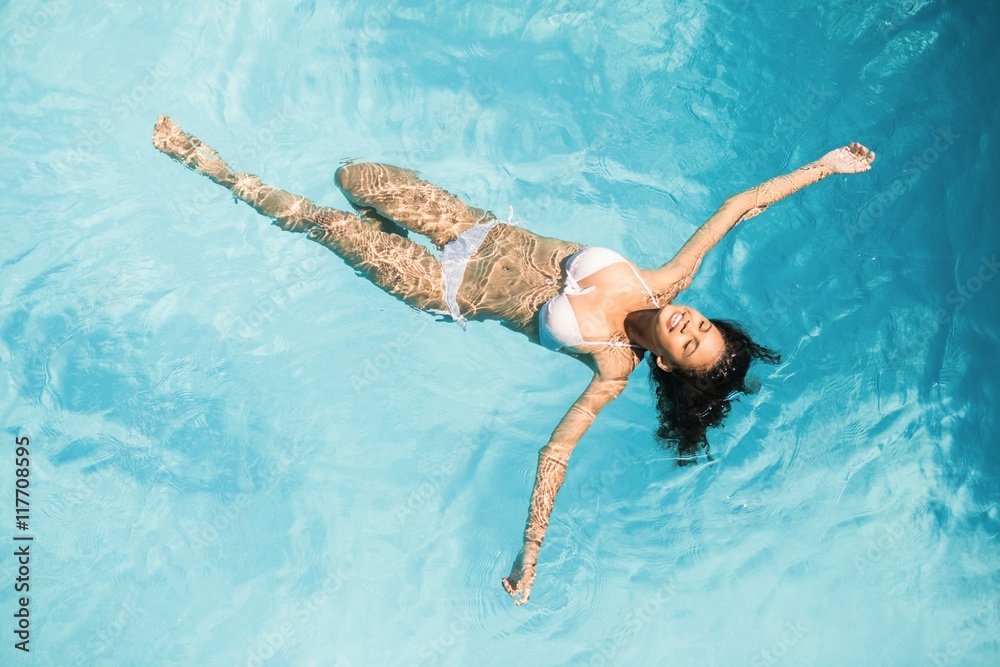 Fototapeta premium Beautiful woman in white bikini floating in swimming pool