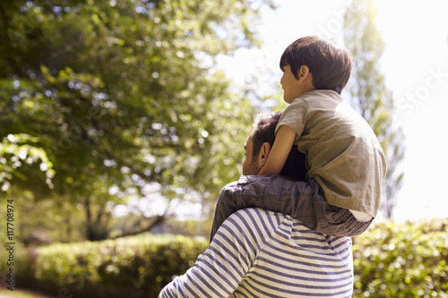 Rear View Of Father Giving Son Ride On Shoulders During Walk