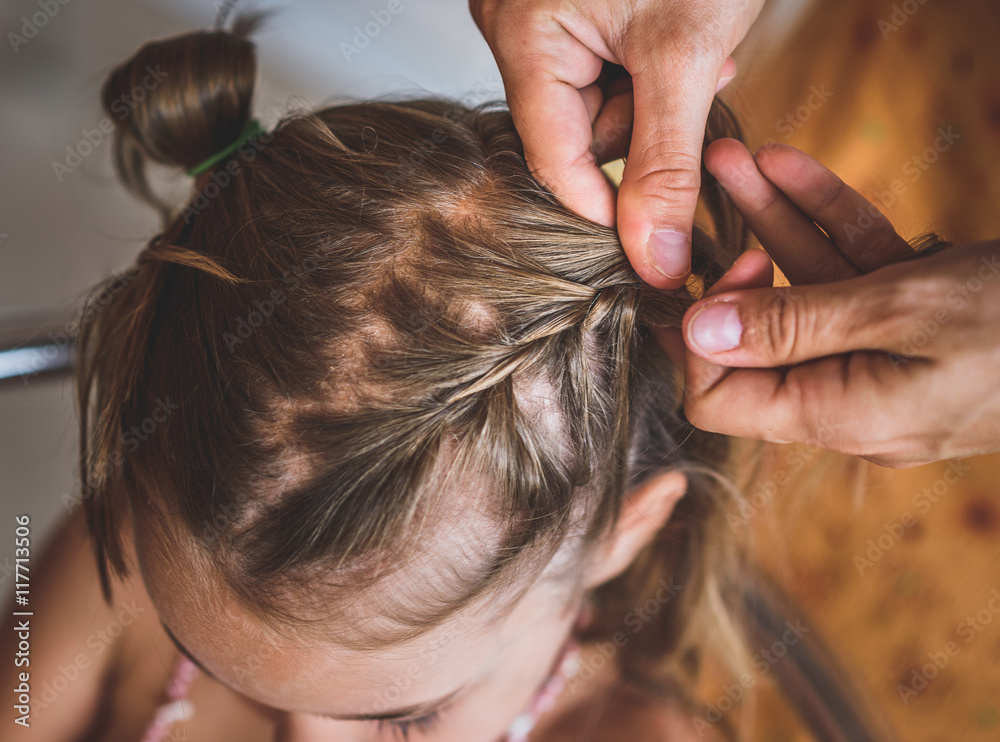 Naklejka premium Mother is making of braids on little daughter's head.