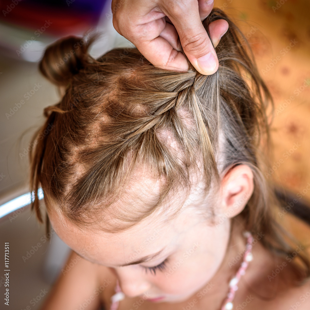 Naklejka premium Mother is making of braids on little daughter's head.