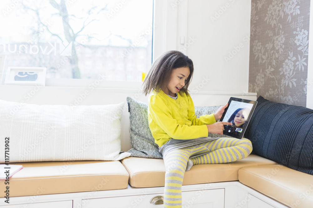 Little girl looking at her photograph on digital tablet in living room Little girl looking at her photograph on digital tablet in living room