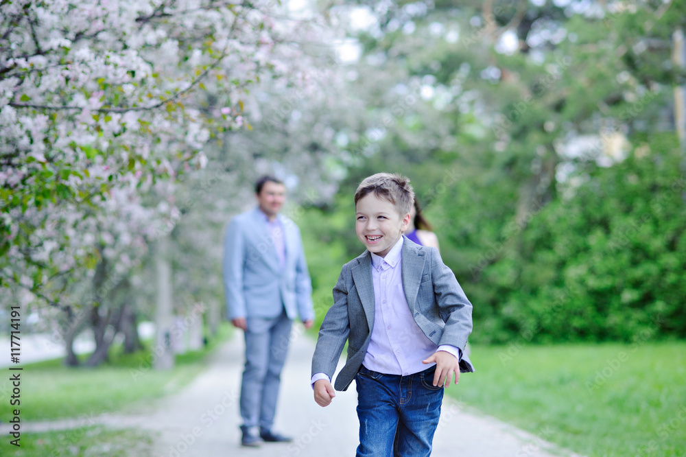 A boy runs along the blooming alleys and laughs in the background are his parents, spring.