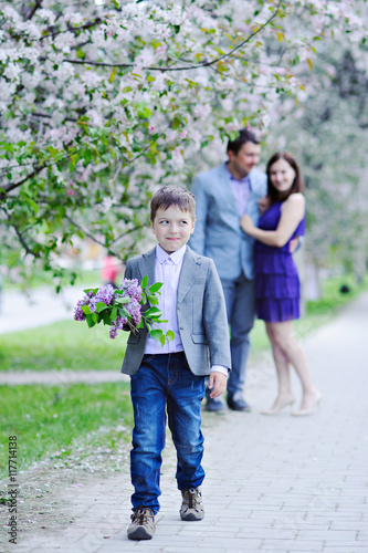 The boy goes with the bouquet of lilacs blooming along the alley and smiles shyly in the background are his parents embracing, full length.