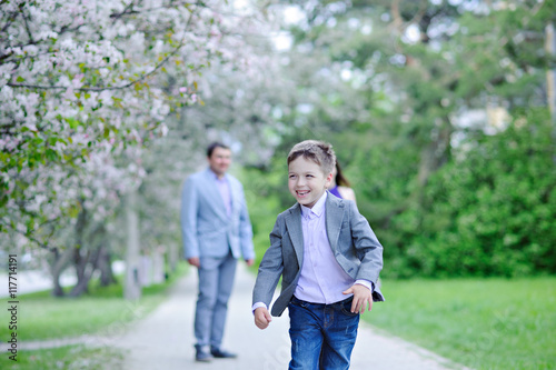 A boy runs along the blooming alleys and laughs in the background are his parents, spring.
