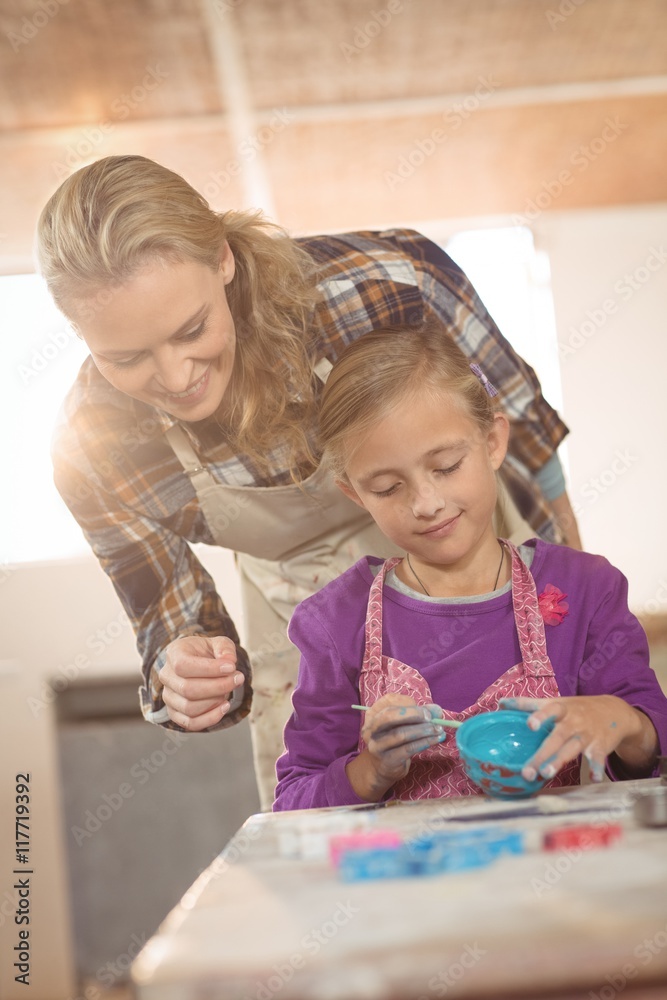 Fototapeta premium Female potter assisting girl in painting at pottery workshop