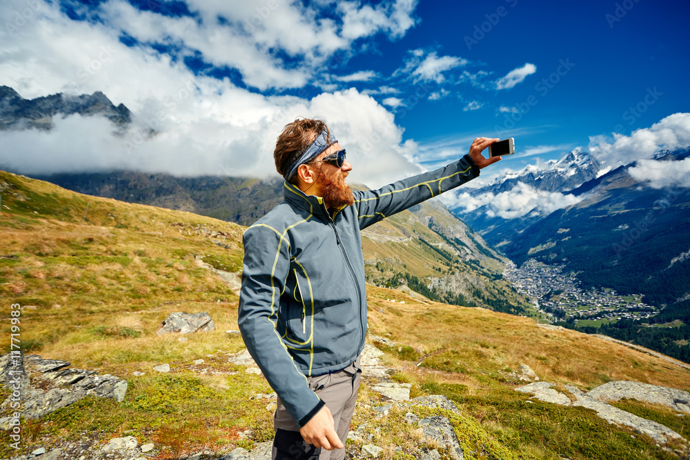hiker at the top of a pass enjoy sunny day in Alps and take photo on smartphone. Switzerland, Trek near Matterhorn mount.