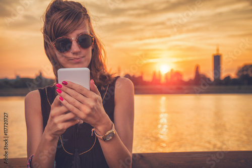 Girl using cellphone on the pier near the river. photo