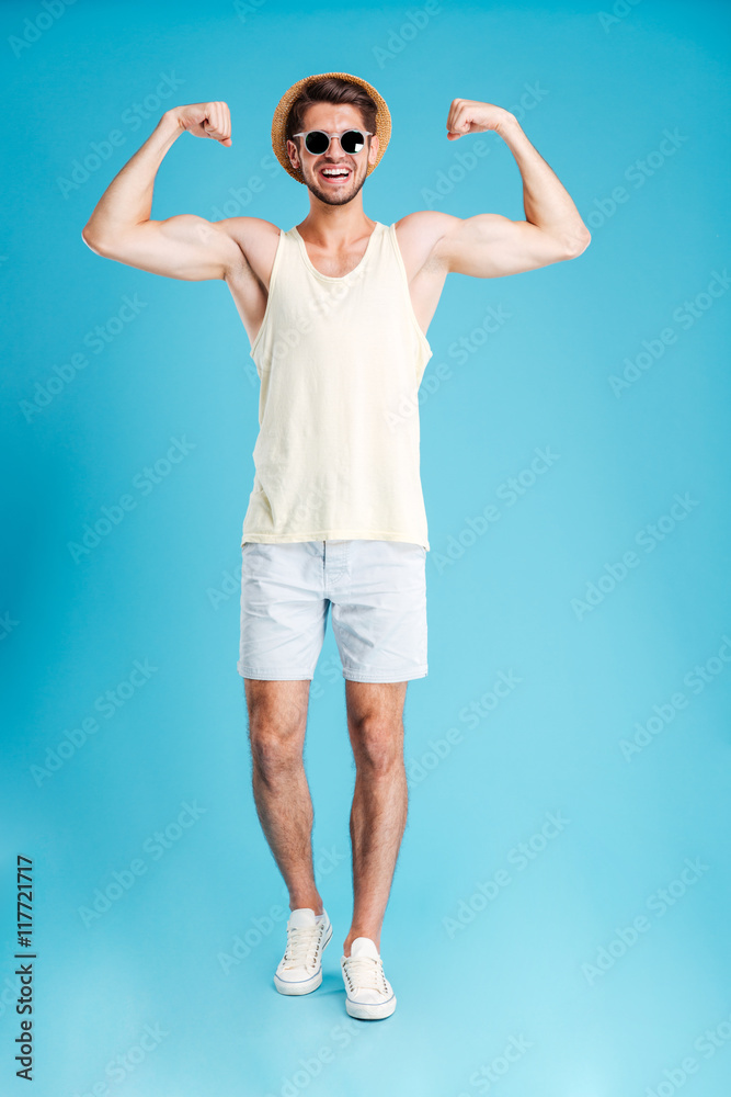 Full length of happy young man standing and showing biceps Full length of happy young man standing and showing biceps