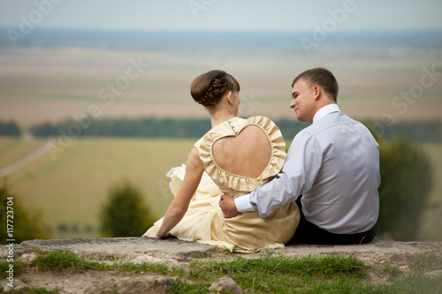 Man sits on the stone with a woman dressing in a gown with open