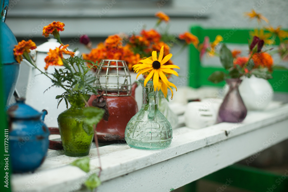 Old glass vases with field flowers stand on the white table