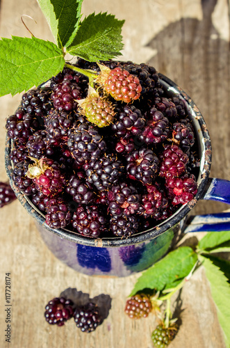 Ripe blackberries and gooseberries in a metal mug on a wooden background closeup. Rustic style, selective focus.  photo