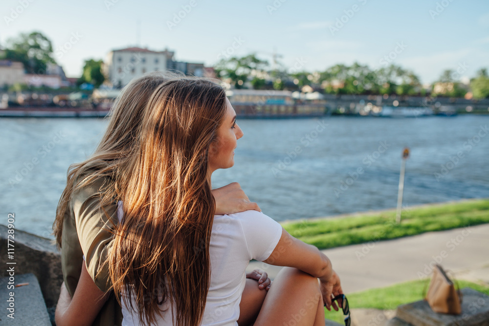 Two young girls sitting on the stairs next to the river and hugg