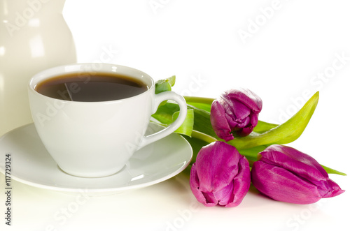 White cup of coffee with bunch of purple tulips on white backgro