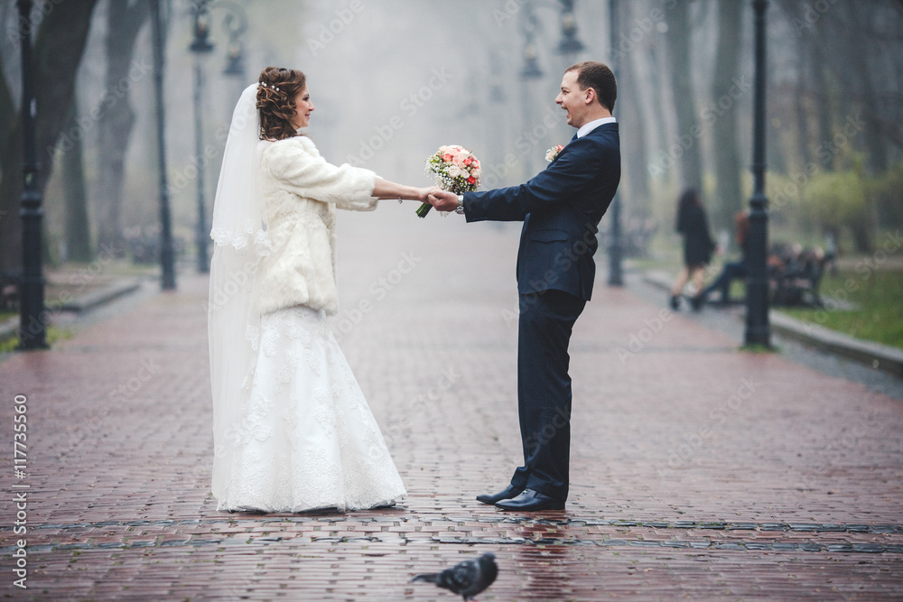 Wedding couple whirls on the wet road in park