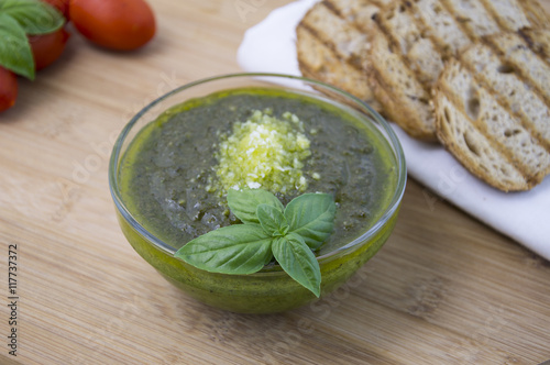 Green pesto with fresh basil leaves in small glass bowl on wooden background