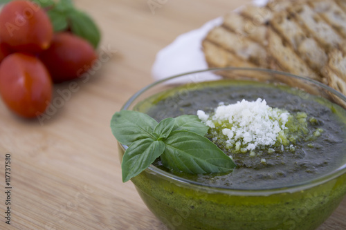 Green pesto with fresh basil leaves in small glass bowl on wooden background