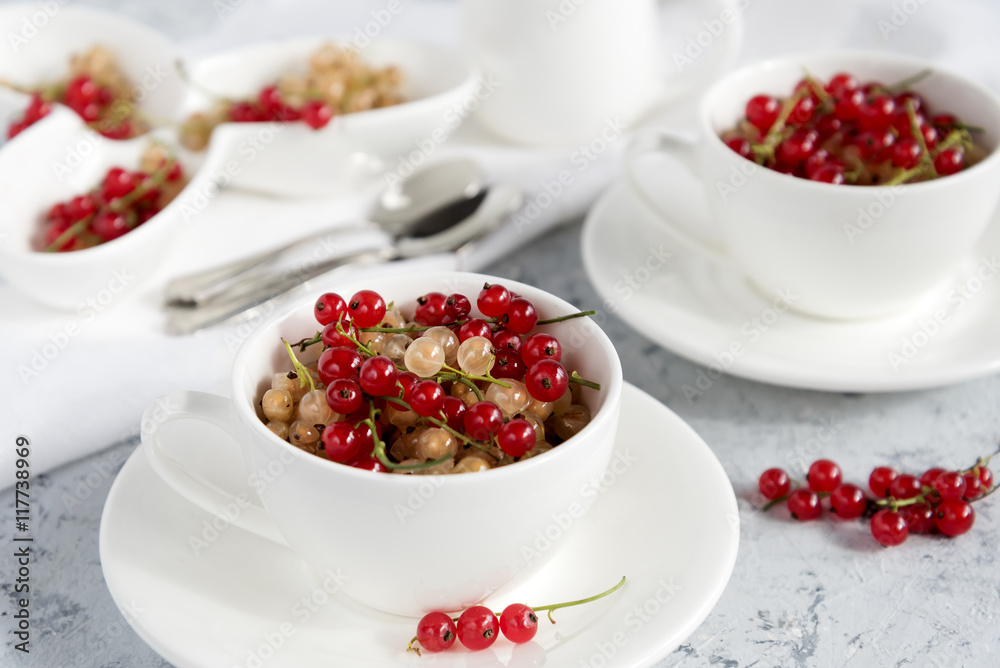 Two white cups with red currant. Light blue background. Horizontal photo. Two white cups with red currant. Light blue background. Horizontal photo.