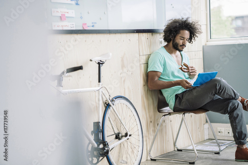 Young designer sitting on chair, eating pretzl and using laptop photo