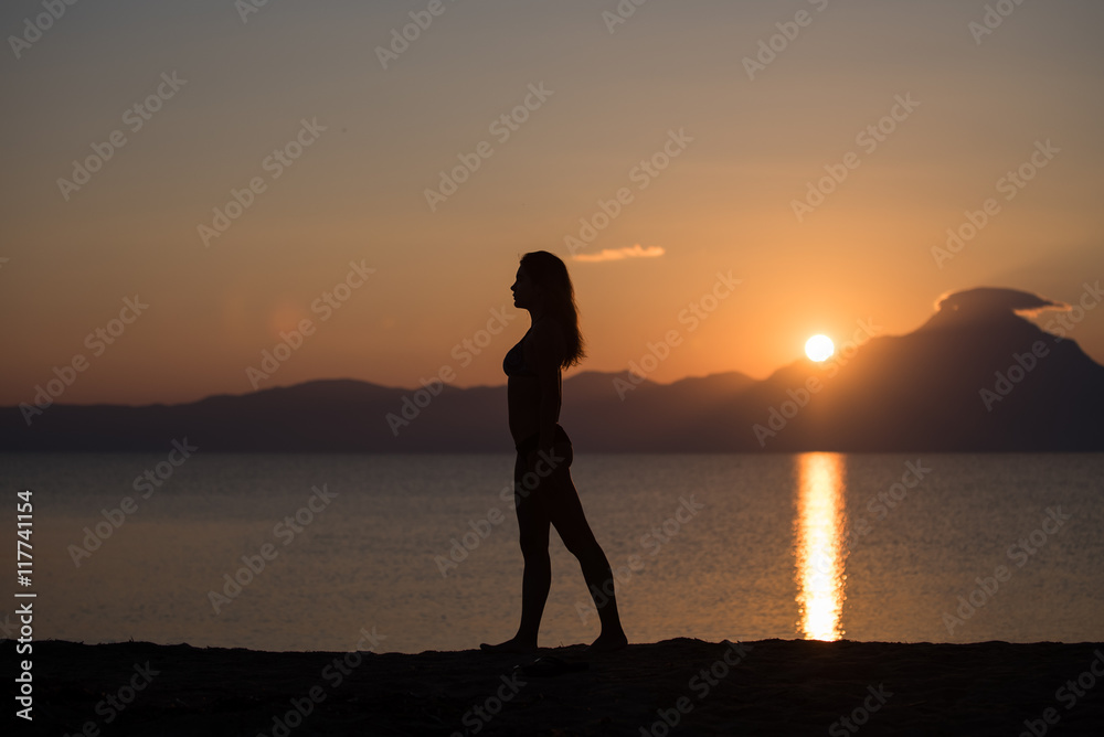 Woman silhouette on the beach at sunrise