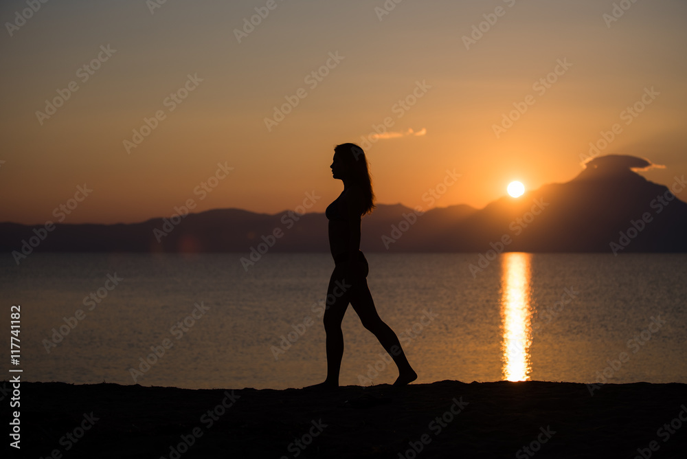 Beautiful woman silhouette on the beach at sunrise