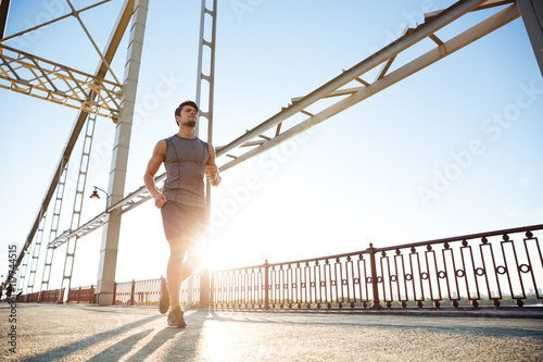 Handsome fit man running fast along big modern bridge