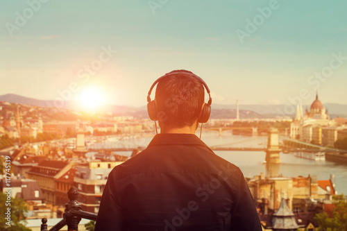 Photography Young man listening music in sunset back view with Budapest