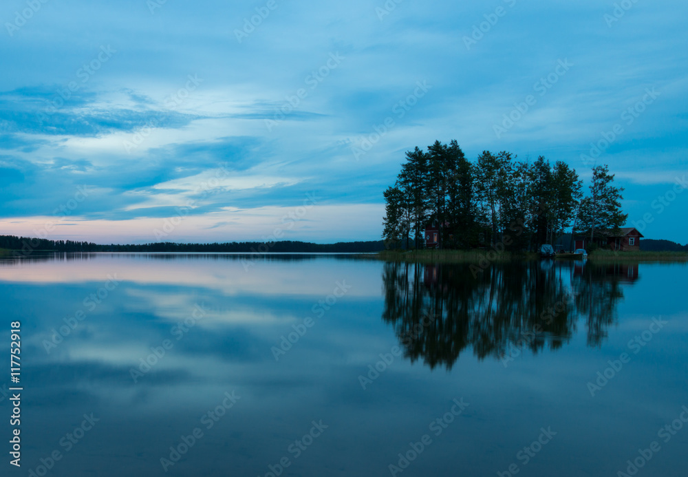 The island in the lake at sunset. The sky in the clouds. The smooth surface of the water.