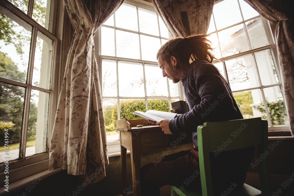 Young man reading book by window at home Young man reading book by window at home