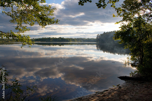 Sunset over the lake in the village. View from the shore in the forest