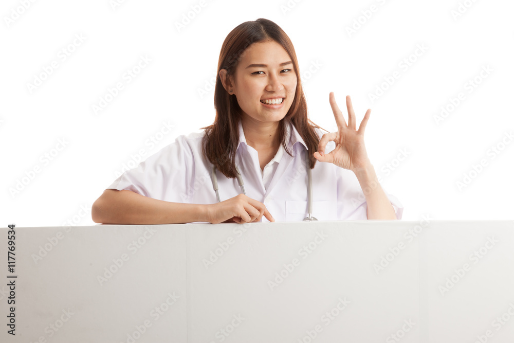 Young Asian female doctor show OK sign behind blank white billb Young Asian female doctor show OK sign behind blank white billb