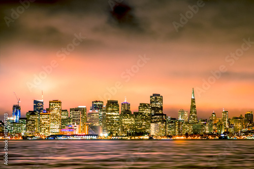 San Francisco California skyline with lights and bay under colorful sunset sky
