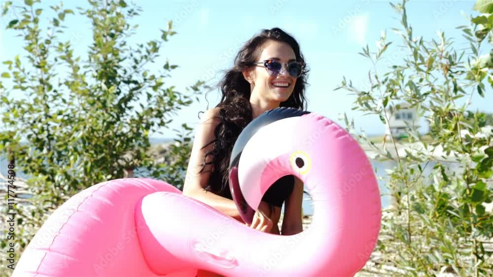 Cheerful beautiful young millennial woman holding sprinkled pink inflatable flamingo float in summer. 20s. 1080p Slow Motion