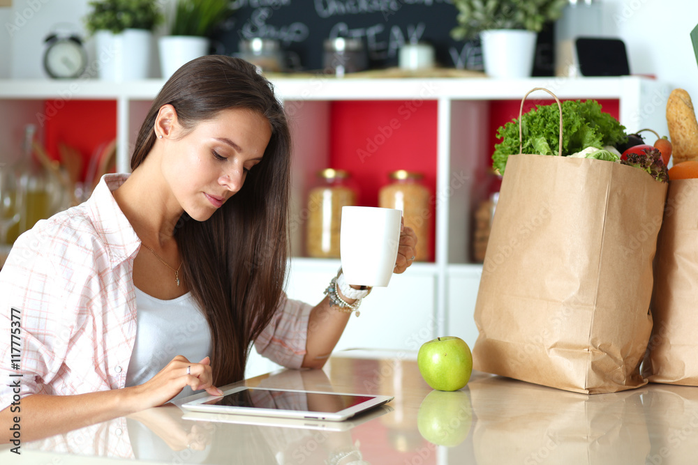 Young woman using a tablet computer to cook in her kitchen . Young woman using a tablet computer to cook in her kitchen .