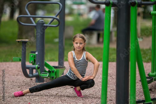 Little sporty girl doing workout on the Playground.