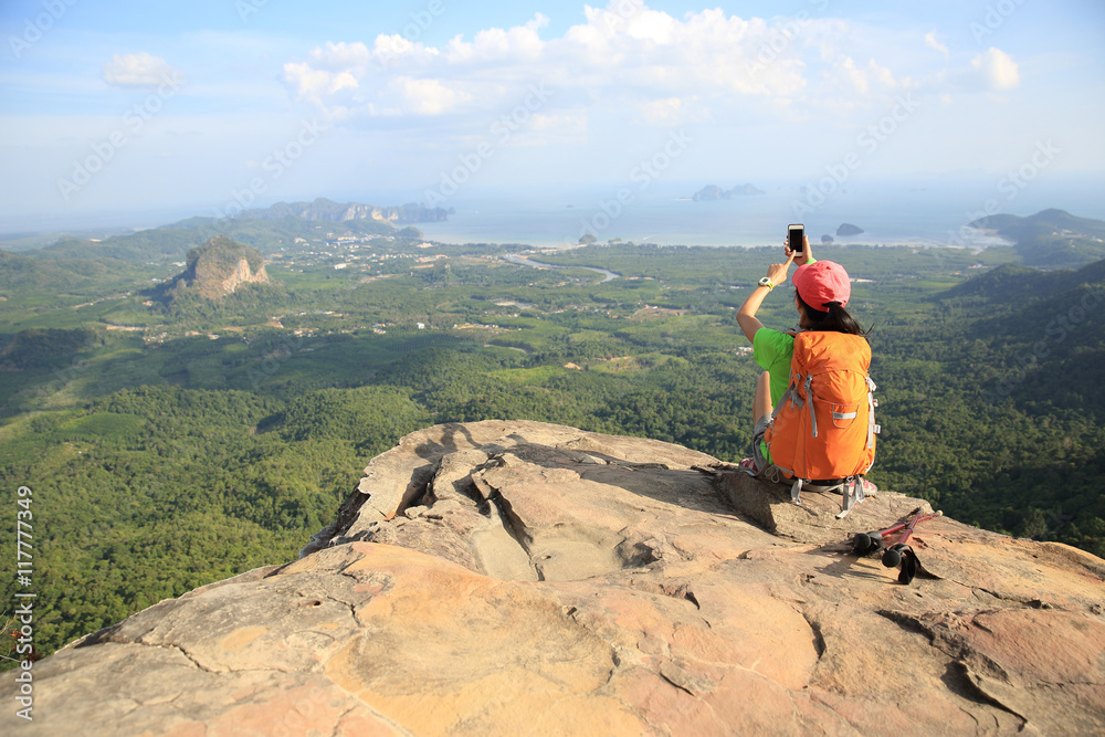 young woman hiker use smartphone taking photo on seaside mountain top