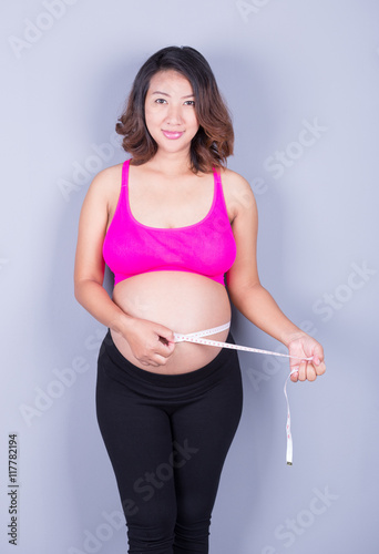 Pregnant woman with measuring tape on gray background © geargodz