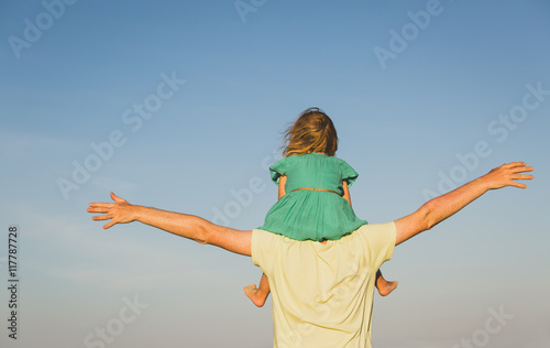 father and little daughter on shoulders play at sky