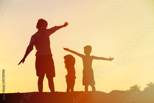father with son and daughter silhouettes play at sunset