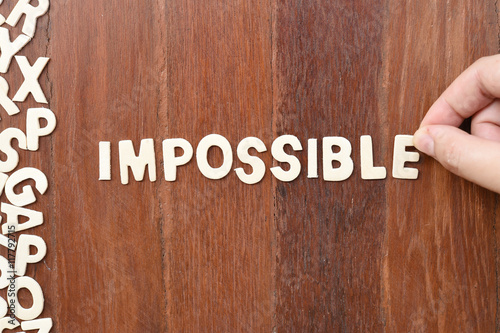 Word impossible made with block wooden letters next to a pile of other letters over the wooden board surface composition