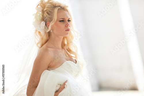 Curly bride looks serious standing in the white room