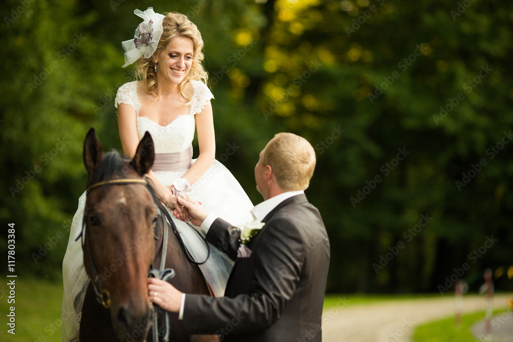 Groom holds bride's hand while she sits on the horse